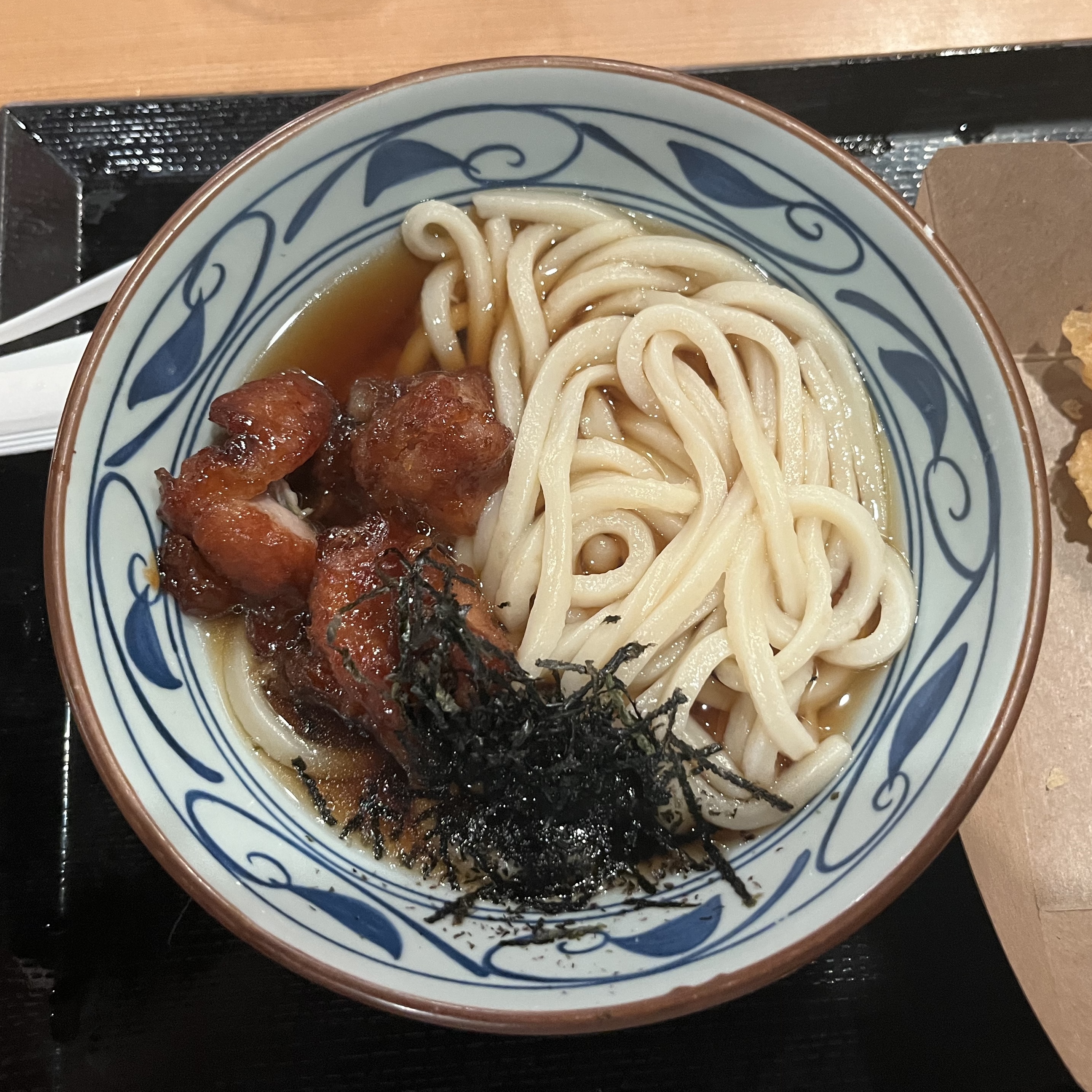 A decorated bowl with udon, chicken, and broth